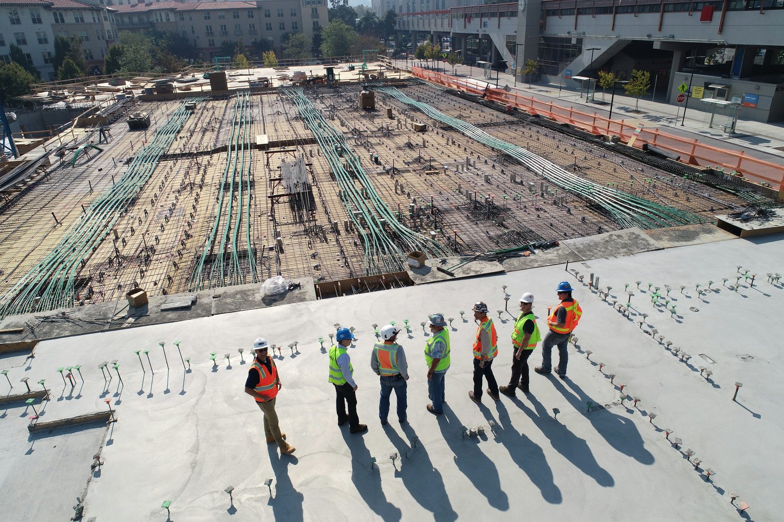 Groupe d’ouvriers en sécurité sur un chantier de construction, debout sur une dalle en béton avec casque et gilet réfléchissant, supervisant des tuyauteries et au loin le site en cours. Travail intérimaire logistique construction.