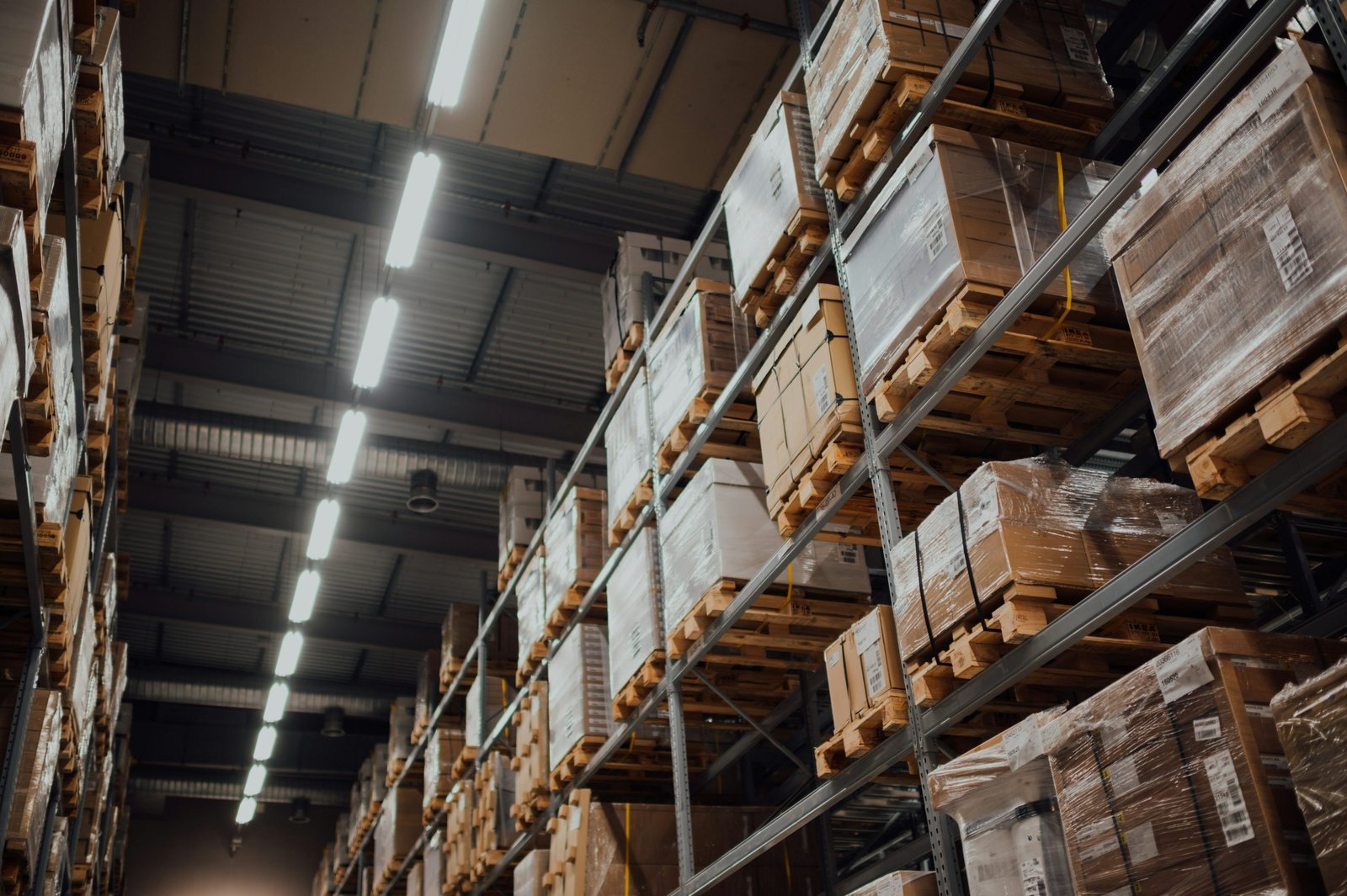Rayonnages en entrepôt remplis de palettes et colis enveloppés, éclairage industriel lumineux. Travail intérimaire logistique construction abordé.