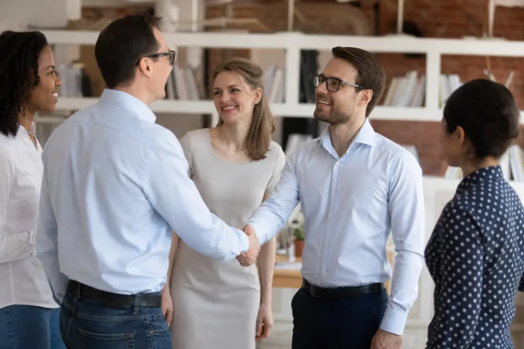 Programme chaleureux d’accueil: deux nouveaux salariés se serrent la main pendant l’onboarding, entourés d’une équipe souriante.