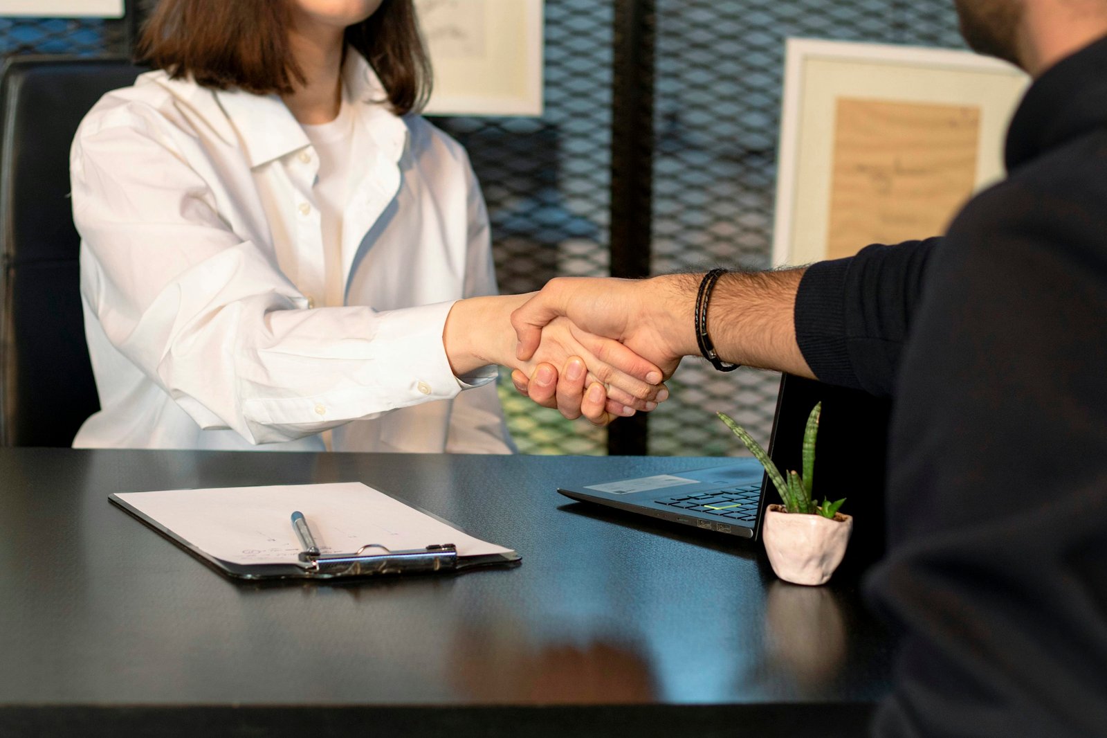 Deux personnes se serrant la main au desk, avec des documents et un ordinateur, symbole d’un onboarding employé réussi.
